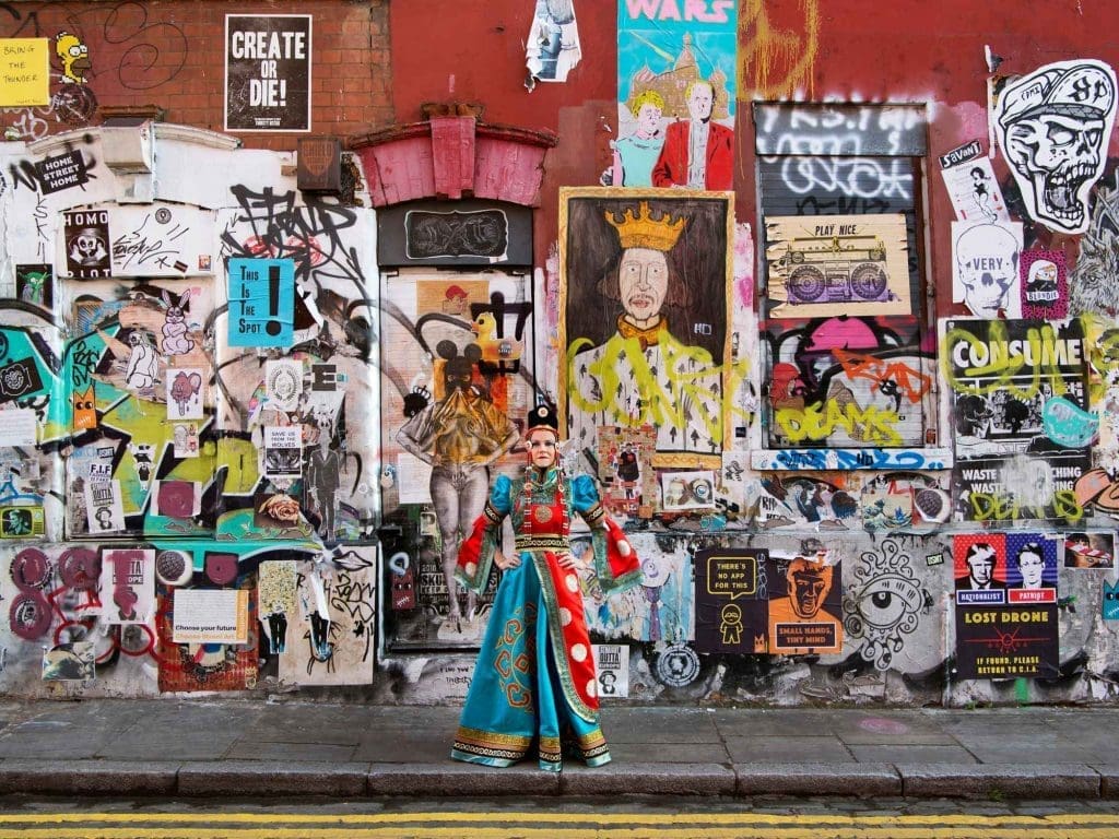 Hilary LANCASTER  Ce portrait me représente telle une «guerrière Urbaine Spirituelle» ; comme quelqu’un qui embrasse les qualités de cou- rage, de force et d’intégrité. J’apporte cette même intégrité et profondeur à mon travail. Lorsque cela s’unit à mon énergie et à ma créativité, nos projets de conception génèrent des intérieurs inspirants et uniques, significatifs et originaux. Ce collage d’art brut de rue à Shoreditch, à l’est de Londres, est provocateur, dynamique et impactant. Ces multiples couches de couleurs et de messages peuvent représenter certains aspects de moi. Le royal et traditionnel costume Mongol que je porte m’impose de régner sur ce ‘Queendom’ de vérité et de liberté créative, et en inspirer les autres à trouver le leur.  Photo : F Ducout